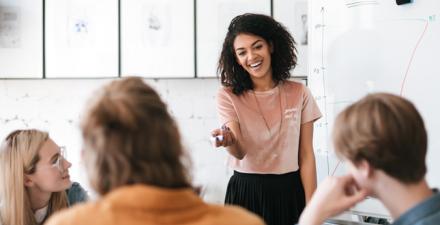 A woman smiles while giving a presentation to a room full of professionals.