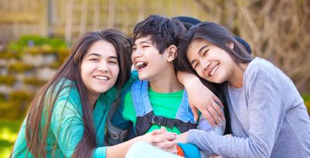 A young boy with cerebral palsy is embraced by his two sisters. 