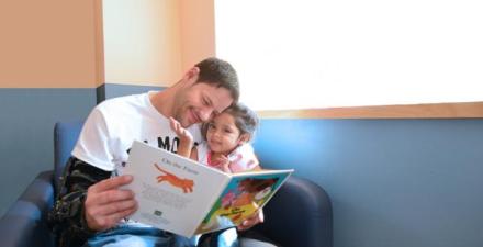 A patient sits with her dad as he reads her a book