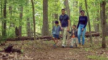 Pictured is Kennedy Krieger patient Dale walking through the woods as he holds hands with his mom, Gina, his dad, Gill, and his little brother, Myles.