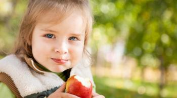 A young girl is holding an apple she has taken a bite out of while sitting outside