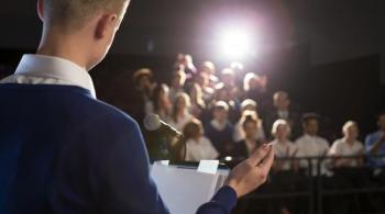 A photograph of a boy standing on a stage and presenting to an audience