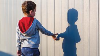 A photo of a child with his back to the camera, touching his shadow reflection