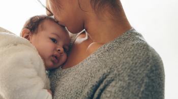 A mother holds her baby, kissing it on its forehead