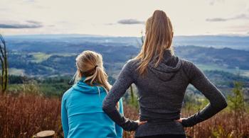 Two women with their backs to the camera look out over a mountain