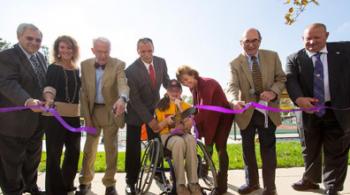 A child in a wheelchair cuts the ribbon in front of a new sports complex.