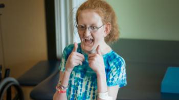 A photo of Ellie, a Kennedy Krieger patient, giving two thumbs up to the camera