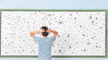 A child stands in front of a board with letters, holding his arms on his head in confusion