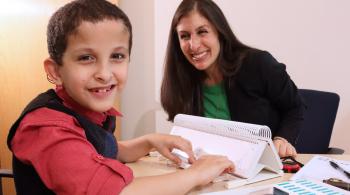 A young patient types on his speech device as he sits with his therapist