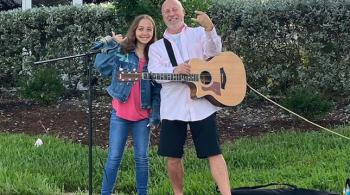 Lola, a young girl, stands next to Mitch, a man. 