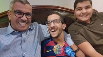 Ali, a father, sits on the sofa with his two adult sons.