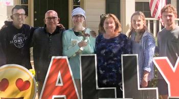 Ally stands with her family behind red and black letters spelling out her name.