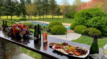 Food and wine sit laid out on a table outside, with rows of colorful trees and nature in the background.