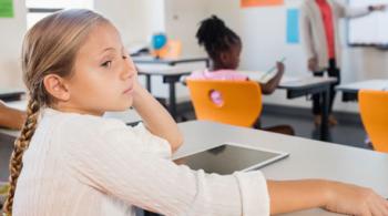 A young girl sits in a classroom, facing away from her teacher.