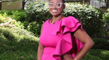 A young woman stands outside. She is smiling and appears confident.