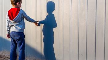 A boy with autism looks at and touches his shadow casted on a wall. 