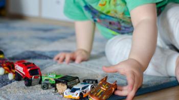 A child plays with small toy cars and trucks in a straight line.