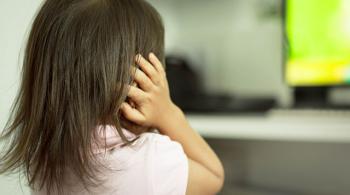 A child afraid of loud sounds covers its ears while standing in front of a tv.
