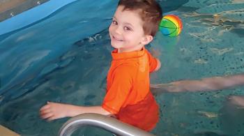 Tripp smiles during aquatic therapy. An inflatable ball floats in the pool behind him.