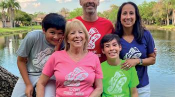 Portrait photo of a family outside, with a pond and palm trees in the background. The family members are Mom, Dad, Grandma and two boys. Each person wears a T-shirt with “Run 4 Cole to cure Sturge-Weber” on it. Each T-shirt is a different color.