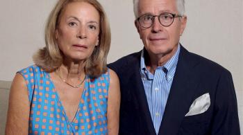 Portrait photo of a woman wearing a dress and necklace and a man wearing glasses and a suit with no tie