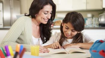 A woman and her daughter read together while sitting at the kitchen counter.