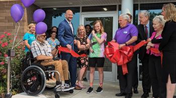 A group of people gathering around a young girl as she cuts a red ribbon to open the International Center for Spinal Cord Injury's White Marsh location.