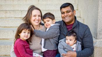 A family portrait of a mother and father, with a little boy and girl, and a baby girl. Everyone but the baby is smiling.