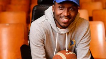 Van Brooks sits in a wheelchair while a football rests in his lap. He is wearing a blue hat with the number 25 in yellow.