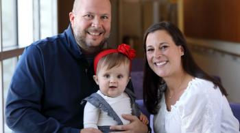 A baby girl sits with her parents.