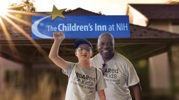 Posed photo of two smiling men in front of a building with a sign that says “The Children’s Inn at NIH.”