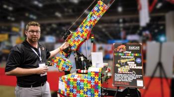 A man stands beside a minicrane, the surface of which is covered with a brightly-colored puzzle-piece design