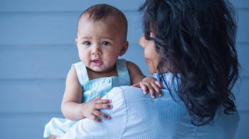 A little baby girl in her mom's arms, against a gray background