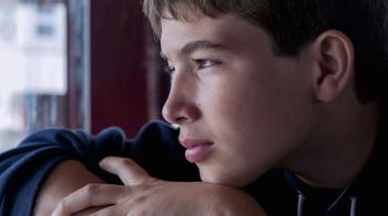 A sad teenaged boy looks out a window. 