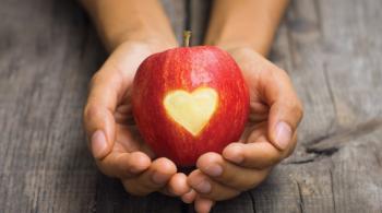 Two hands cusp a red apple with an engraved heart.