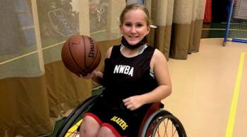 Liza, a Bennett Blazer adaptive athlete, holds a basketball on a basketball court.