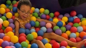 A young girl sits in a ball pit and smiles.