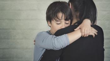 Sad child hugging his mother against a light brick background