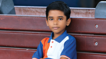 A boy sits on a bench with his arms folded across his chest.