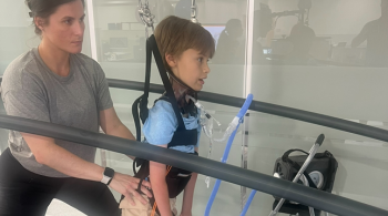 A child participates in a TSS session on a treadmill as their physical therapist stands behind them.