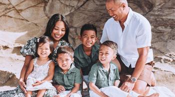 A posed family photo with two parents, three little boys and a little girl. The family appears to be sitting in a rocky setting, and they are wearing muted greens and natural colors.