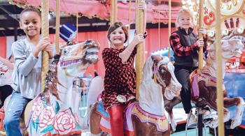 Three little girls smile while riding a carousel at Kennedy Krieger's annual Festival of Trees.