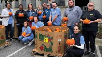 A group of volunteers hold small pumpkins outside of Kennedy Krieger Institute.