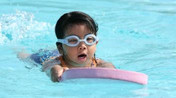 A boy swims in a swimming pool while using a paddle board.