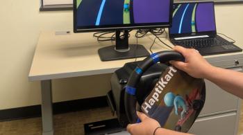 A child plays the HaptiKart video game, using a steering wheel as the control. Only their hands are visible.