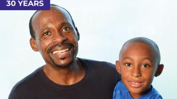 A father and son smile for the camera. The son is about 5 years old and appears to be wearing a Superman T-shirt.