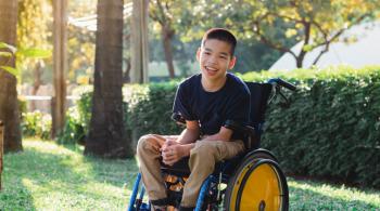 A boy smiles while sitting in a wheelchair.