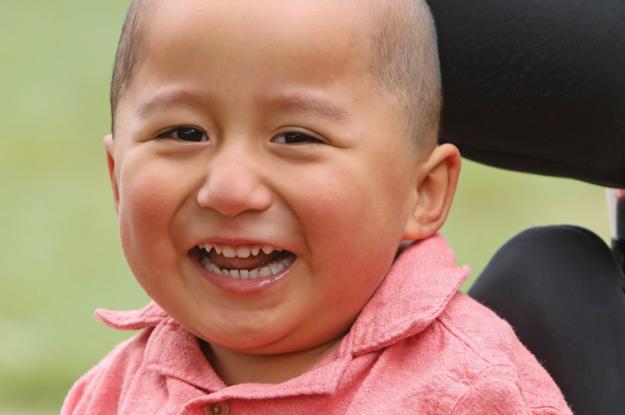 A young boy sitting in a wheelchair smiles.