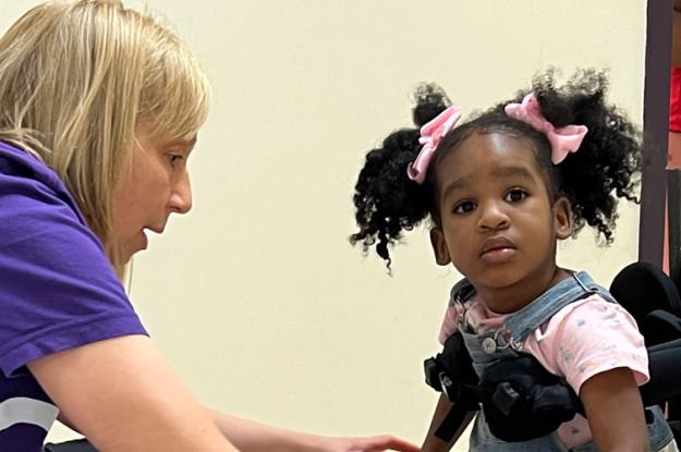 A physical therapist assists a little girl who is using a mobility device.