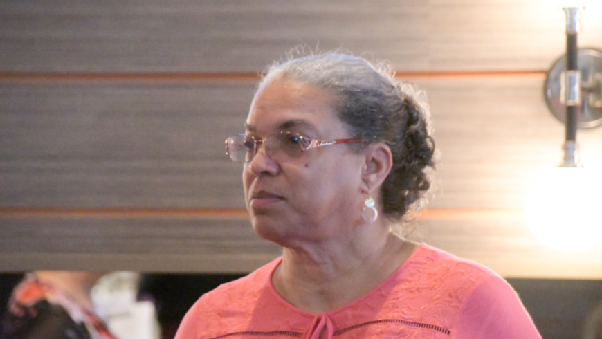 Closeup image of a woman wearing a pink shirt, facing to the right of the camera.